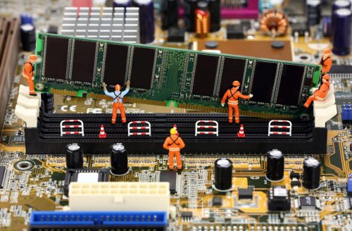 Miniature construction workers installing RAM memory on a computer motherboard.